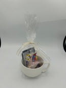 A gift set featuring a large white mug, a packet of hot cocoa mix, a black and white cookie, two small chocolate squares, and a bag of mini marshmallows.