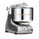 A sleek, modern Ankarsrum Assistent Original stand mixer in a dark grey and silver finish, featuring a large stainless steel bowl with "ANKARSRUM" embossed on it, and two control knobs on the front panel.