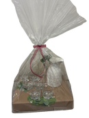 A beautifully wrapped gift set featuring a white hammered pitcher with a silver handle and six clear glass tumblers, elegantly arranged on a neutral-toned base with greenery accents. Encased in clear cellophane and tied with a soft pink ribbon, this set is a stylish and practical gift.