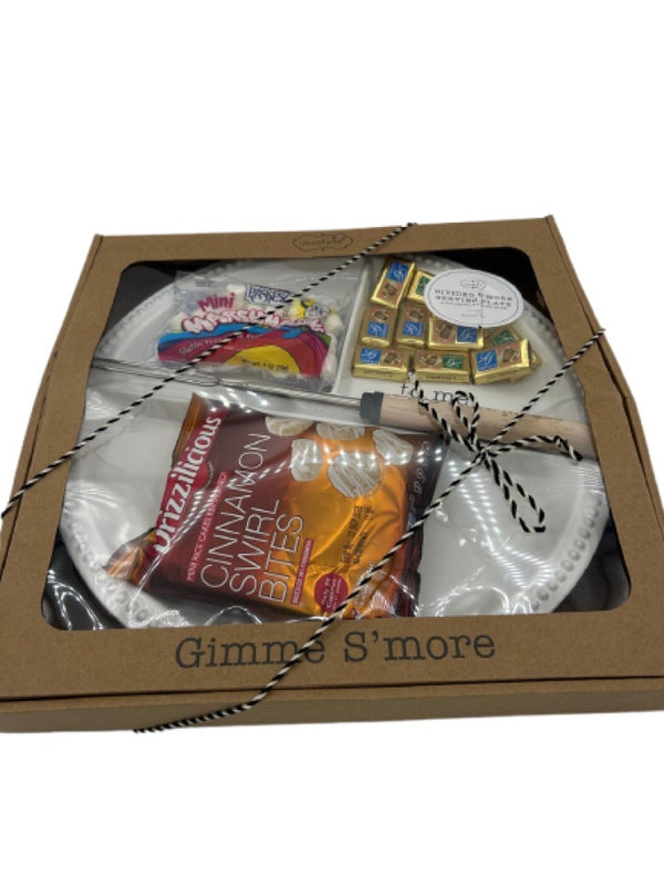 A beautifully packaged Shalach Manos gift set labeled ‘Gimme S’more,’ featuring a Mud Pie divided s’mores serving plate with a roasting fork, a bag of Paskesz Mini Marshmallows, Drizzilicious Cinnamon Swirl Bites, and Alprose Napolitain Chocolates. The set is elegantly tied with black and white twine, making it a perfect Purim gift.