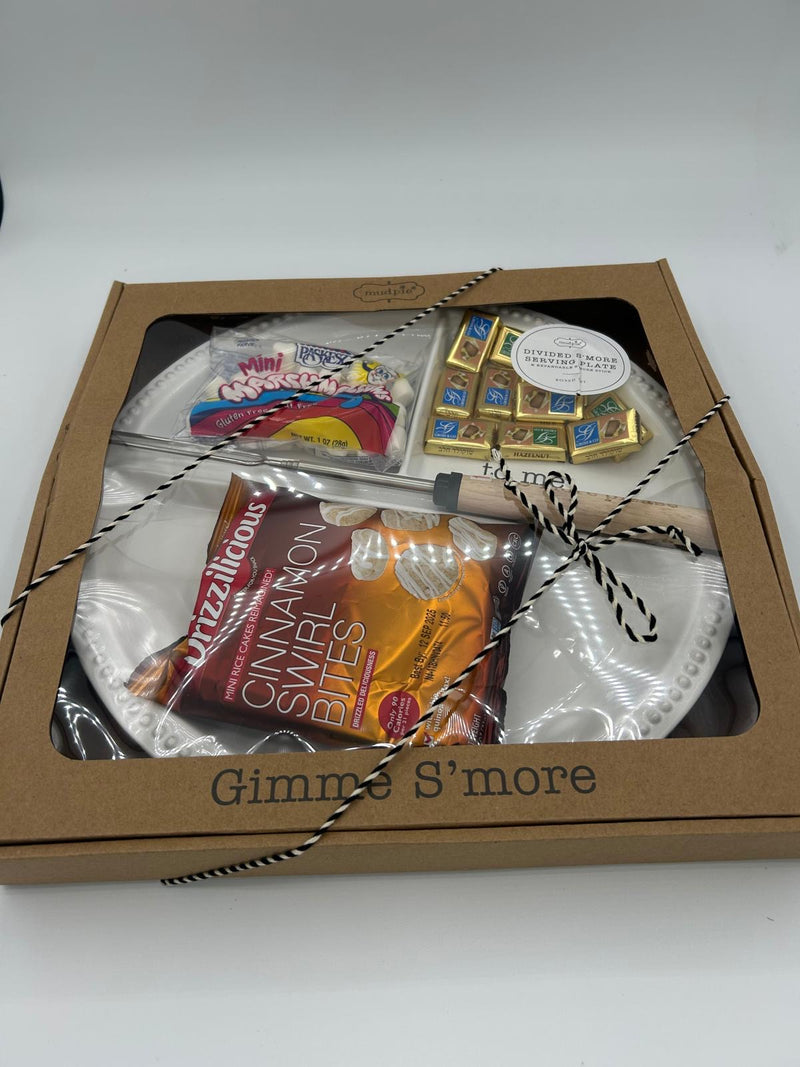 A close-up of the ‘Gimme S’more’ Shalach Manos gift set, showcasing a neatly arranged selection of s’mores essentials, including a ceramic divided serving plate, a roasting fork, gourmet chocolates, marshmallows, and cinnamon swirl bites. The packaging is sleek and gift-ready, wrapped with twine for a festive touch.