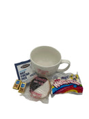 A gift set featuring a large white mug, a packet of hot cocoa mix, a black and white cookie, two small chocolate squares, and a bag of mini marshmallows.