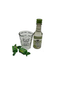 A mini bottle of Smirnoff Green Apple Vodka (50ml), a Fox Run 1.5 oz Measuring Shot Glass, and two sour green apple candies.