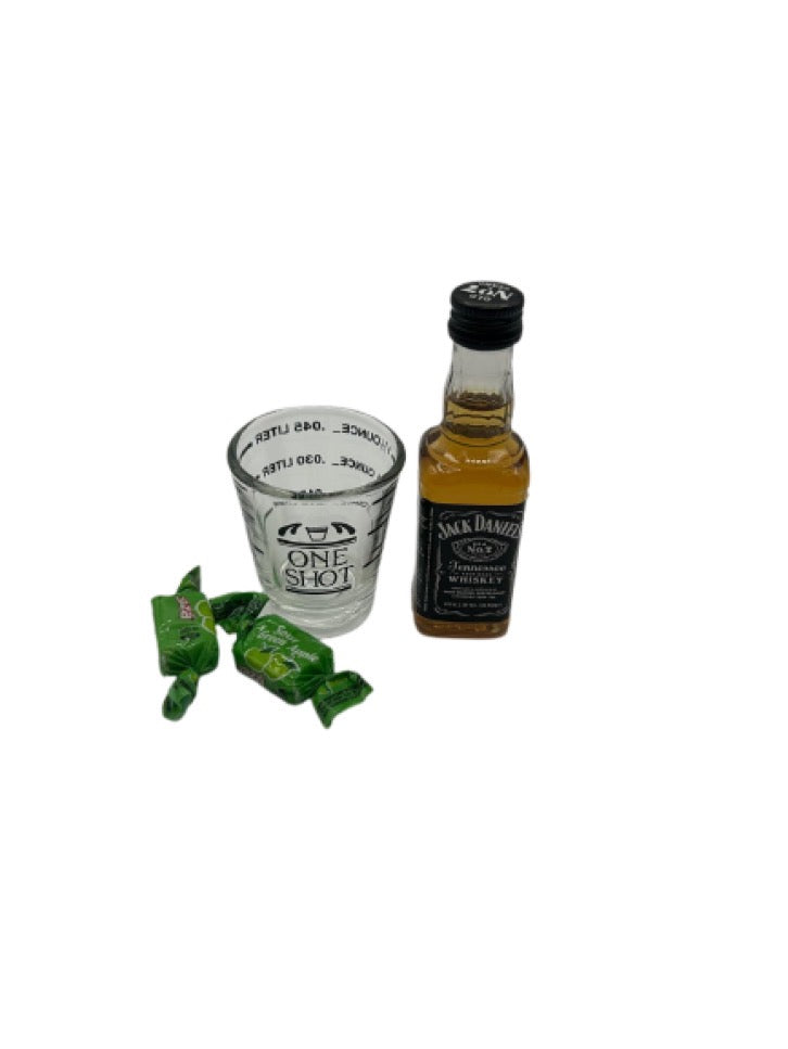 A mini bottle of Jack Daniel’s Tennessee Whiskey (50ml), a Fox Run 1.5 oz Measuring Shot Glass, and two Sour Green Apple Candies placed neatly on a white background.