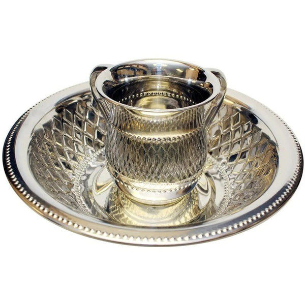 A silver Netilat Yadayim washing cup with an intricate diamond-cut design, paired with a matching silver plate featuring a beaded rim.