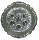 A round, silver-plated Seder plate with a highly ornate scalloped border and intricate engravings. The plate has seven depressions, each with an engraved Hebrew word.
