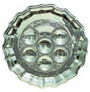 A round, silver Seder plate with a scalloped edge and six depressions for the Seder foods. Each depression is engraved with a Hebrew word. The plate has intricate decorative engravings.