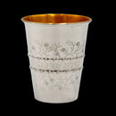 A shiny, silver-plated Kiddush cup and matching plate set. The cup has a gold interior and is engraved with a floral design and Hebrew text. The plate has a decorative border.