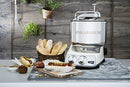 A countertop bread maker with freshly baked baguettes and pastries nearby, set against a rustic wooden backdrop with greenery.