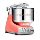 Premium Ankarsrum Original kitchen machine with a vibrant coral or peach-colored base and large, polished stainless steel mixing bowl, ideal for baking and food preparation. This durable stand mixer features chrome accents and a front control panel with two dials for easy operation.