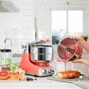 Premium Ankarsrum Original kitchen machine with a vibrant coral or peach-colored base and large, polished stainless steel mixing bowl, ideal for baking and food preparation. This durable stand mixer features chrome accents and a front control panel with two dials for easy operation.