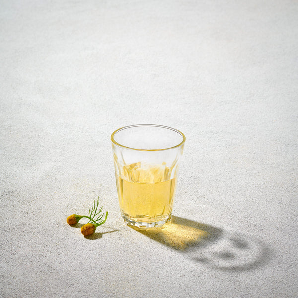 A LAV 3.75oz clear glass wine tumbler, filled with a light golden beverage, set on a neutral background with olives as garnish.