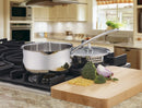 stainless steel saucepan resting on a stove near a counter with some chopped vegetables