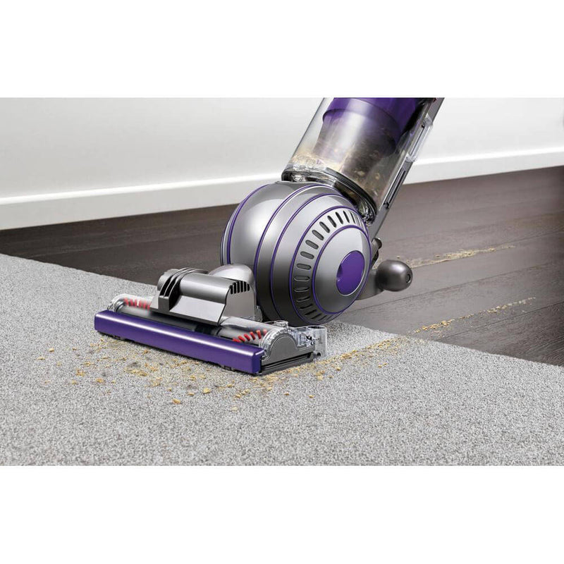 Dyson vacuum cleaning carpet with visible debris pickup.