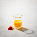 Clear 6.5oz glass filled with orange juice next to a fresh strawberry on a light textured surface