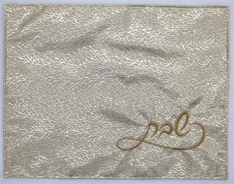 Elegant white challah cover with subtle floral pattern and gold embroidered Hebrew text reading "Shabbat"