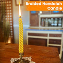 Yellow braided Havdalah candle displayed upright in a decorative holder, captioned “Braided Havdalah Candle.”
