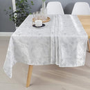 A stylish, silver tablecloth drapes over a wooden table, complemented by a tray with glasses and a candle in a modern dining setting.