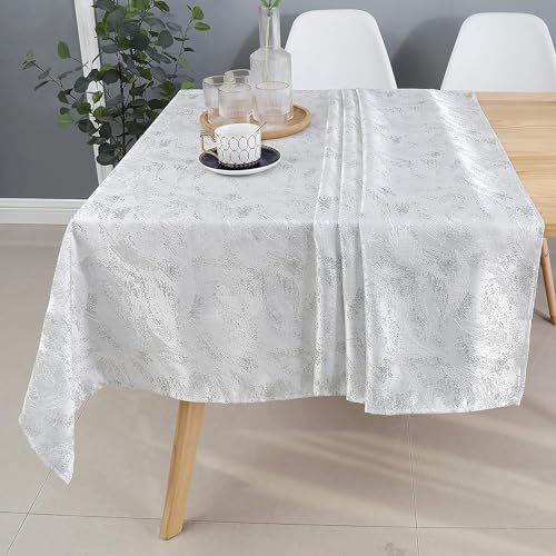Elegant white tablecloth draped over a wooden table, featuring a decorative pattern, with a candle and glasses on a tray.