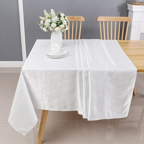 A white tablecloth drapes over a wooden table, with a vase of flowers in the center and two wooden chairs on either side.