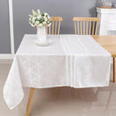 A neatly arranged dining table with a white geometric tablecloth, featuring a vase of flowers and wooden chairs in a modern setting.
