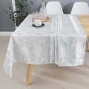 A silver damask rectangular tablecloth draped over a dining table with white chairs.