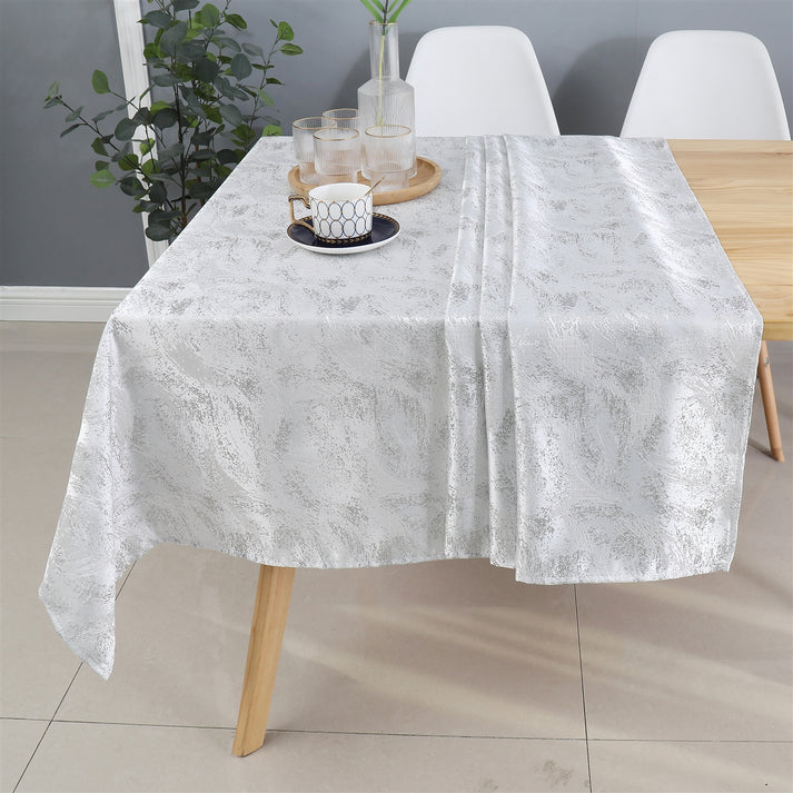 Silver floral tablecloth spread across a dining table with decor