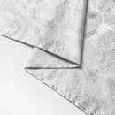 Close-up of folded silver fabric with a subtle, textured pattern, elegantly draped over a white surface.