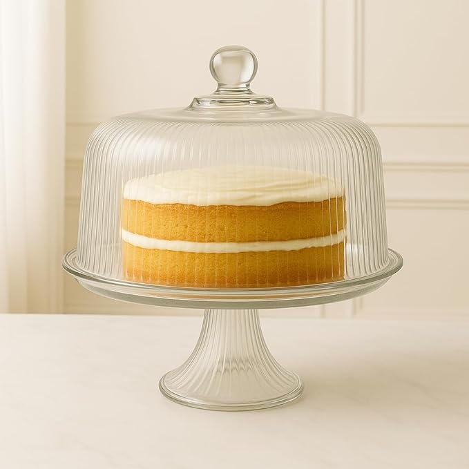 Cake displayed under glass dome on clear pedestal stand in a white setting