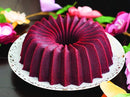 red Bundt cake with defined ridges, sitting on a white plate atop a wooden table,
