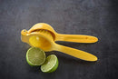Yellow lemon squeezer with halved lime on dark countertop