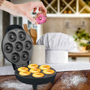Mini donut maker in a kitchen setting with a hand placing a decorated donut on top.