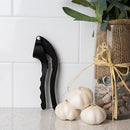 Black garlic press displayed upright next to garlic bulbs on a kitchen counter