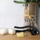 Black garlic press resting on a countertop beside whole and minced garlic