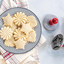 Cookies shaped using the Nordic Ware set of three silver cast aluminum cookie stamps with red wooden handles, piled on a plate on a table