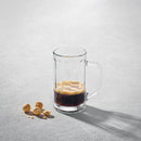 Clear glass beer mug with handle filled with dark beverage on a light surface