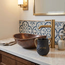 Black and gold polymer wash cup sitting on a bathroom counter next to a sink