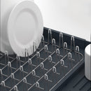 A gray Joseph Joseph Expandable Dish Drying Rack with a removable white cutlery holder and a plated steel wire rack for dishes. The rack is shown in its compact size.