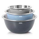 Three OXO Good Grips stainless steel mixing bowls nested inside each other, showing their gray, light blue, and dark gray exteriors and shiny stainless steel interiors. Each bowl has a white OXO logo and appears to have a non-slip base.