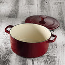 A red enameled cast iron round casserole with matching lid and wide handles, shown on a wooden table