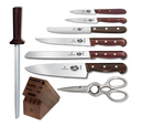 A high-angle studio shot displays a professional Victorinox knife set, including a dark wood knife block, a sharpening steel, a pair of stainless steel kitchen shears, and five different types of knives, all with dark wood handles, arranged neatly on a white background.