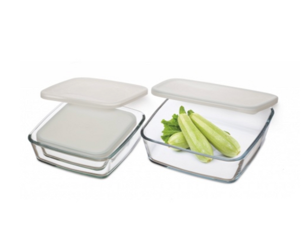Two clear square glass food storage containers with off-white lids; one is empty and stacked, the other holds green vegetables.