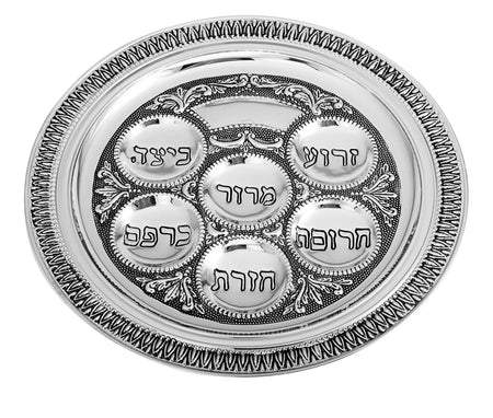 A decorative silver Seder plate with six compartments, each labeled in Hebrew for Passover symbols. Intricate border design.