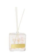 Elegant home fragrance diffuser in a clear glass bottle, showcasing preserved light pink and white flowers and accompanied by white diffuser sticks.
