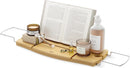 A light wood Umbra bathtub caddy with expandable metal arms, featuring a slotted book/tablet stand, a wine glass holder, and a recessed area with drain holes for soap or accessories.