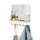 A sleek white wall-mounted mirror with rounded corners, featuring a light wood shelf beneath it. Below the shelf, a white bar extends with several wooden peg hooks.