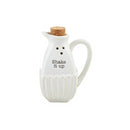 A white ceramic shaker shaped like a miniature pitcher/cruet. It has a fluted bottom half, a small spout, a cork stopper, and the black text 'Shake it up' on the side.