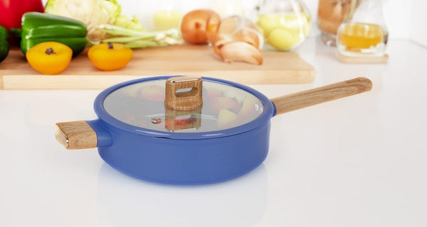 Stylish blue saucepan with a glass lid and wooden handles, placed on a white countertop with fresh vegetables and ingredients in the background. Ideal for modern kitchens and cooking enthusiasts.