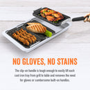 Grilling and serving set by Yukon Glory, featuring a large silver pan and three smaller black grill/sear trays with cooked food, plus a handle, all next to its product packaging.