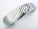 A sleek, stainless steel garlic press with a unique curved shape and perforated crushing surface.